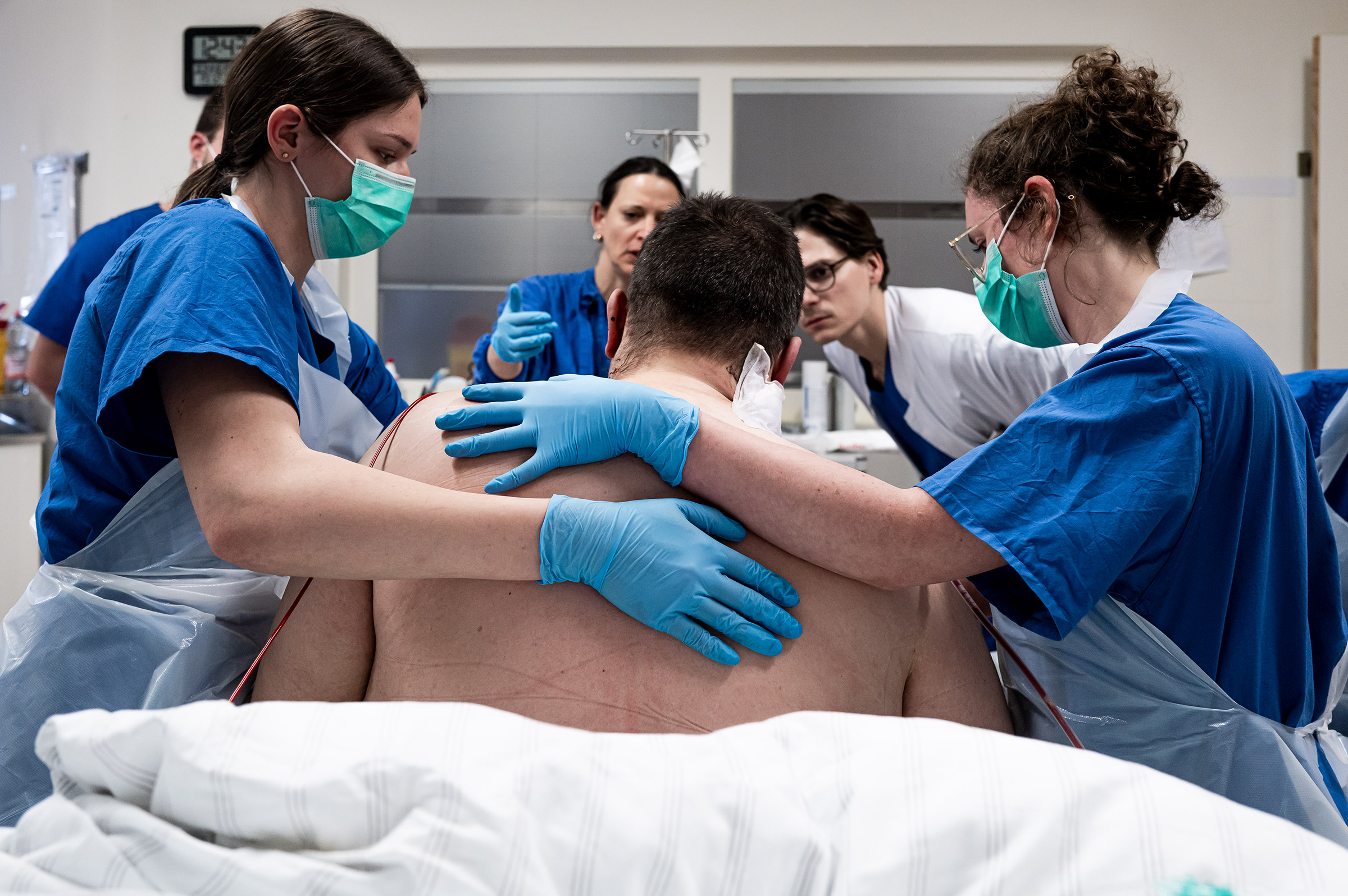 Ärzte begutachten einen Patienten, der von Pflegern gehalten wird. Mehrmals am Tag geht eine Gruppe von Ärzten durch die Station, um sich einen Eindruck von den Patienten zu machen. 