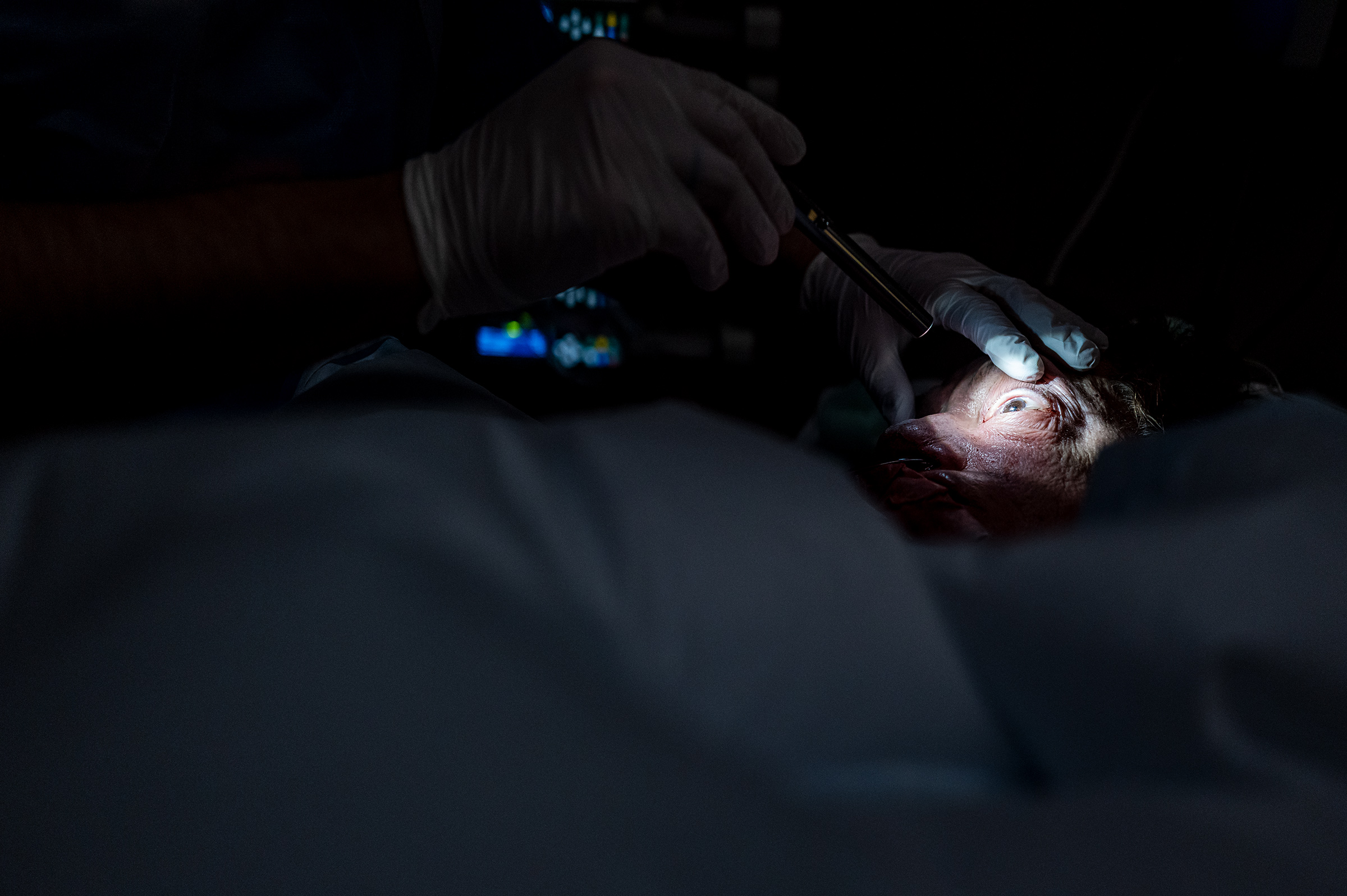 Ein Intensivpfleger beleuchtet das Auge eines Patienten. Damit wird getestet, ob und wie die Pupille reagiert, da es Rückschlüsse auf den Gesundheitszustand geben kann. 